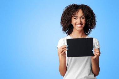 Değerlendirmeler, teklifler ve online başvurular. Kıvırcık saçlı, kar beyazı tişörtlü mutlu Afro-Amerikan kadın. Mor arka planda izole edilmiş, boş ekranlı tablet gösteriyor.