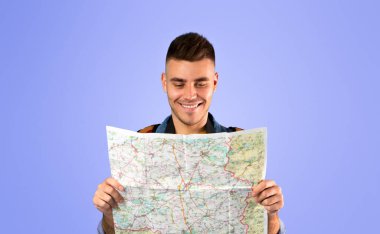 Modern kameralı genç turist mavi arka plandaki haritaya bakıyor.