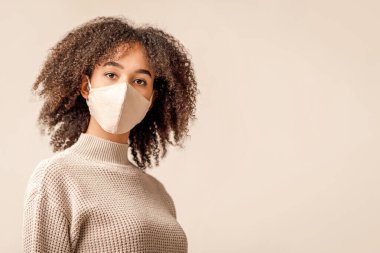 Yeni normal ve karantina sonrası yaşam, salgın sırasında sağlığını korumak. Beyaz arka planda izole edilmiş koruyucu maskeli ve süveterli Afro-Amerikan bayan portresi.