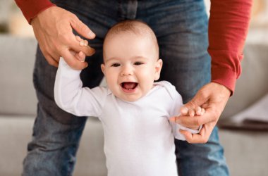 Babacığın küçük bebek yürüyüşüne ve eve ilk adımlarını atmasına yardım ediyor. Mutlu Yürüyen Bebek, Babaların Ellerini Kapalı Tutuyor. Sevimli Babalık Anları Konsepti. Kırpılmış