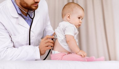 Sağlık kontrolünden. Hastanede steteskop kullanarak akciğerlerini dinleyen kızı muayene eden doktor. Küçük hasta klinikte pediatri randevusu alıyor. Çocuk Sağlığı Konsepti. Kırpılmış