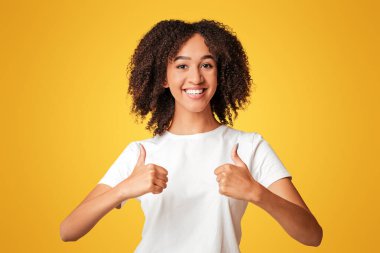 Harika eleştiriler ve mutluluk duygularını ifade ediyor. Afro-Amerikalı genç bir kadının portresi gülüyor, parmaklarını turuncu arka planda izole edilmiş kameraya gösteriyor, stüdyo çekimi, serbest alan