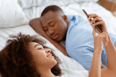 Rahatlayın, uyuyun ve sabah yatağınızda bir aletle uyanın. Gülümseyen Afro-Amerikan kadın akıllı telefonda sörf yapıyor, internette haberler okuyor, gündüzleri uyuyan kocasıyla, kapatıyor, mekanı kopyalıyor.