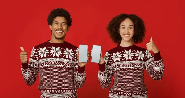 Yeni yılı ve Noel 'i aynı kıyafetlerle kutlamak. Mutlu binlerce yıllık Afro-Amerikan çifti ekranları boş akıllı telefonları kırmızı arka planda, panoramada, stüdyo çekimlerinde gösteriyorlar.