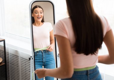 Kilo kaybı. Mutlu Kız Bel Bantlı Ölçüyor Evde Ayna İncelenen Önünde Duruyor. Boşluğu Kopyala, Seçici Odaklanma