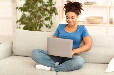 Mutlu Afrikalı Amerikalı serbest çalışan kadın dizüstü bilgisayarda çalışıyor, internette para kazanıyor evde koltukta oturuyor. Uzak İnternet İşi ve Serbest Yaşam Tarzı Konsepti. Boş Alan