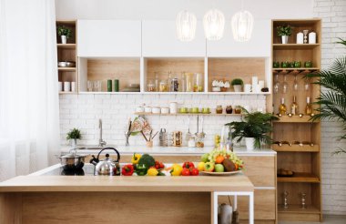 Ahşap mutfak, ada ve büyük masa. Meyve ve sebzeler masada.