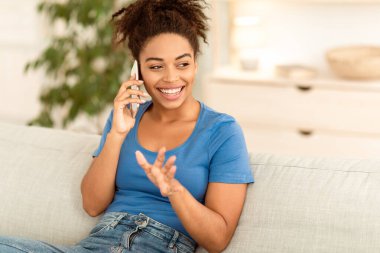 Evdeki koltukta oturan mutlu Afrikalı Amerikalı kadın cep telefonuyla konuşuyor. Telefon Görüşmesi Konsepti