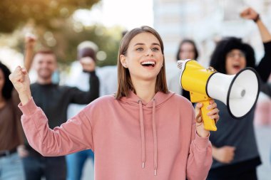 Tutkulu sarışın kadın eylemci, sokakta megafonla sloganlar atıp yumruğunu kaldıran, uluslararası aktivist grubuna önderlik eden neşeli genç kadın, kilit altına alma kurallarına karşı geliyor.