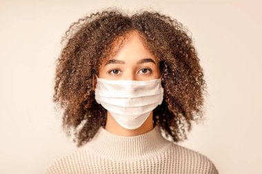 Virüsü ve salgın hastalıkları durdurun, yeni normal ve covid 19 karantinayı durdurun. Üzgün Afro-Amerikan kadın koruyucu maskeli, kameraya bakıyor, yakın çekim, ışık kremi arka planında soyutlanmış.