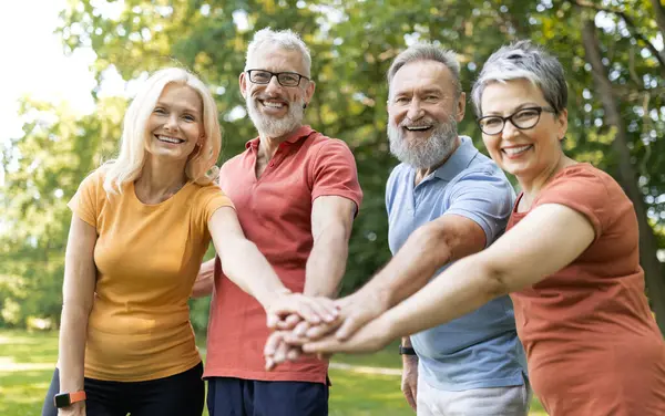 Bir grup neşeli son sınıf öğrencisi spor üstüne spor yapıyor mutlu yetişkin erkekler ve kadınlar avuç içlerine katılıyor ve dışarıda antrenman yaptıktan sonra başarıyı kutluyorlar.