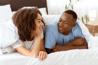 Hafta sonları birbirinizle iletişimin tadını çıkarın ve karantina sırasında evinizde dinlenin. Binlerce yıllık neşeli Afro-Amerikan çifti örtülü, kadın yatak odasında erkek dinleyin, boşluğu kopyalayın