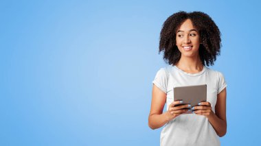 Çalışma ve öğrenim teknolojisi. Bin yıllık gülümseyen Afro-Amerikan kadın, elinde tablet, online alışveriş yapıyor ve mor arka planda izole edilmiş boş alana bakıyor.