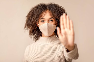 Kadın hasta, maske takıyor ve sosyal mesafeye uyum sağlıyor. Koruyucu maskeli Afro-Amerikan kadının yüzüne odaklan, el örgüsü ile çevrilmiş, arka planda izole edilmiş, stüdyo çekimi