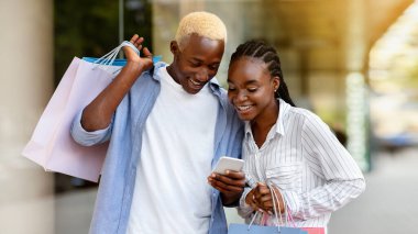 Akıllı telefondan satışla ilgili reklam. Gülümseyen Afro-Amerikan adam ve kiz kese kağıtlariyla sehir merkezindeki telefona bakiyorlar.