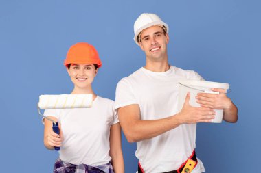 Stüdyoda boya kovası ve paten fırçasıyla poz veren birkaç tamirci, ev yenileme ve duvar boyama için hazır gülümseyen adam ve kadın,