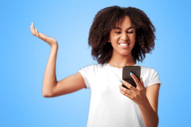 Çıldırmak, sinirlenmek ve online oyunda kaybetmek. Duygusal açıdan bin yıllık Afrikalı Amerikalı kadın akıllı telefona bakıyor ve hayal kırıklığını ifade ediyor. Mor arka planda izole edilmiş, stüdyo çekimi.