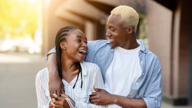 Boş zaman, eğlence ve alışveriş. Gülümseyen Afro-Amerikan çifti, gündelik kıyafetleriyle alışveriş merkezinin yakınında, açık havada, boş alanda sarılıyorlar.
