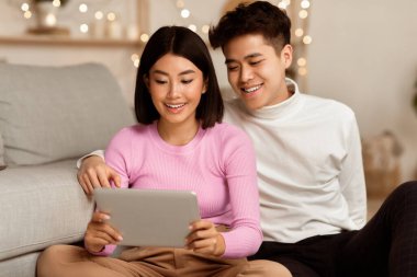 Neşeli Asyalı çift tablet bilgisayar kullanıyor. İnternette film seyrediyor. Evde yerde dinleniyor. Birlikte Hafta Sonu Boş Zaman, Modern Aile Yaşam Tarzı.