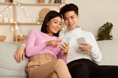 Koreli eşler cep telefonlarını internet taraması ve evdeki koltukta oturan uygulamaları tavsiye ediyor. Haftasonu Birlikte Akşam Geçiren Akıllı Telefonlu Çift.