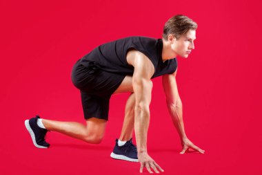 Güçlü milenyum atleti kırmızı stüdyo arka planı, yan görüş üzerinde başlangıç pozisyonunda. Yakışıklı genç sporcu başlangıç çizgisinde, koşmaya hazır, tam boy portre