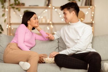 Japon çift, hafta sonunu evde koltukta oturup patlamış mısır yiyerek geçirmekten keyif alıyor. Akşam Evde Kalma, Romantik İlişki, Flört ve Flört Konsepti.