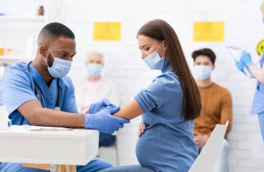 Coronavirus aşısı. Hastanedeki Covid-19 'a karşı aşılanan yüzü maskeli hamile kadın. Afro-Amerikan Doktor Corona Virüs Aşısı Enjekte Ediyor Hastaya. Kapalı Korunma