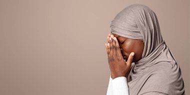 Üzüntülü, tesettürlü, elleri tesettürlü, siyah İslamcı kadın, depresif, başörtüsü takmış, arka planda duran, utanmış, profil portresi fotokopi uzayı olan bir kadın.