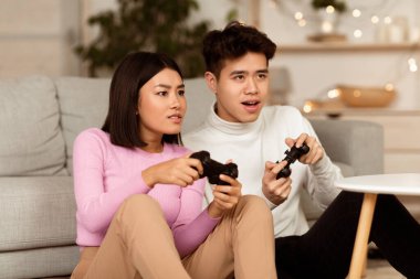 Çinli çiftler bilgisayar oyunu oynuyorlar. Oyun çubukları tutuyorlar. Hafta sonları evde oturup eğleniyorlar. Asyalı Erkek Arkadaş ve Kız Arkadaşı Akşam Video Oyunu Oynuyor