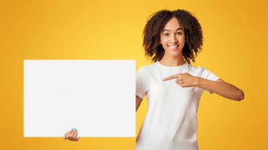 Reklam alanı ve müşteri tavsiyesi. Kıvırcık saçlı, boş yeri olan pankartı tutan ve sarı arka planda izole edilmiş, gülümseyen Afro-Amerikan kadını.