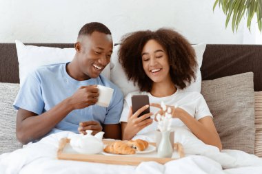 Haberler, sosyal ağlar, harika bir teklif ve yatakta kahvaltıda reklam. Binlerce yıllık Afro-Amerikan çifti ellerinde fincanlar, çay içiyorlar, kruvasan yiyorlar ve telefonda yatak odasında komik videolar izliyorlar.