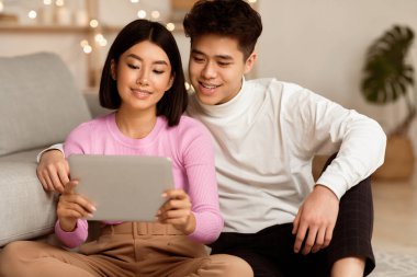 Japon aile çifti dijital tablet kullanıyor. İnternette film izliyor. Oturma odasında dinleniyor. Asyalı Kız Arkadaş ve Erkek Arkadaşı Bilgisayar Haftasonu Gecesini Birlikte Geçiriyor