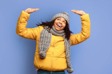 Neşeli siyahi kız kaldırılmış ellerle bir şeyleri yukarı itiyor ya da kafasının üstünde duran görünmez bir nesneyi tutuyor. Mor stüdyonun arka planında duruyor.