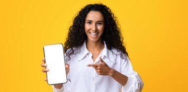 Smartphone 'u siyah ekranla gösteren neşeli esmer kadın, yeni uygulamayı gösteriyor, sarı arka planda izole edilmiş, tasarım için boş alanı olan, reklam için yaratıcı şablon