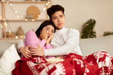 Japon aile çifti televizyon seyrediyor ve TV 'de korkunç bir film seyrediyor evde battaniyeyle oturmuş Noel' i kutluyorlar. Noel Arifesi Eğlence Konsepti.