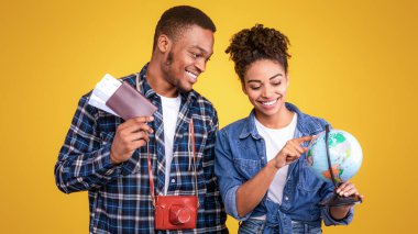 Turizm. Afro-Amerikan Gezgin Çifti Gezgin Gezgin İstikametini Seçiyor Dünyayı Bekleme ve Biletleri Sarı Stüdyo Arkaplanı Üzerinde Pozlandırıyor