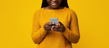 Smiling African American Lady Holding Smartphone, Texting With Friends On Yellow Background, Cheerful Black Female Using Cellphone, Enjoying Modern Technologies And Mobile Communication, Copy Space