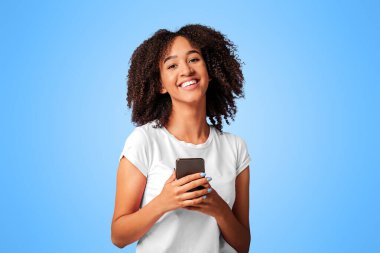 Modern cihazlar, binyıllar ve başarı duyguları. Neşeli Afrikalı Amerikalı bayan gülüyor, akıllı telefonu tutuyor ve yeni cep telefonu uygulaması kullanıyor, menekşe arka planda izole edilmiş, stüdyo çekimi, boş alan,