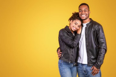 Sarı Stüdyo Arkaplanında Duran Kameraya Gülümseyen Mutlu Siyah Çift. Kız arkadaş ve erkek arkadaş kucaklaşması. Aile, Aşk, Romantik İlişki Konsepti