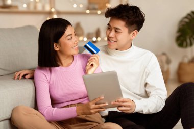 İnternetten alışveriş. Hafta sonları evde oturan Asyalı çift internet mağazasında sipariş için dijital tablet ve kredi kartı kullanıyor. Mutlu Müşteriler, E-Ticaret Konsepti