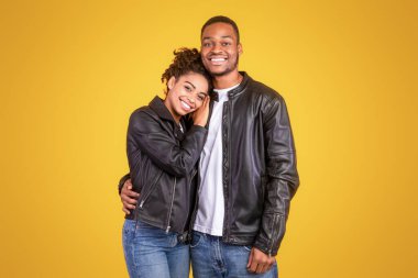 Siyah deri ceketli, sarı arka planda duran ve kameraya gülümseyen Afrikalı çifte bayılıyorlar. Stüdyo çekimi. Romantik İlişki Konsepti. Boş Alanı Olan Panorama