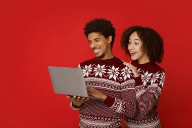 Noel indirimi ve internet üzerinden eğlenceli bir görüşme. Şaşırmış ve mutlu genç Afro-Amerikan ailesi dizüstü bilgisayara bakar ve ailesiyle iletişim kurar, kırmızı arka planda izole olur, stüdyo çekimi yapar.
