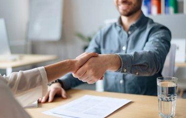 İnsan kaynakları müdürünün ofisteki boş kontenjan başvurusuyla el sıkışması, yakın plan. Tanımlanamayan kafa avcılığı uzmanı yeni çalışanı şirket ekibine kabul ediyor.