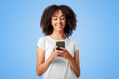 Modern cihazlar ve çevrimiçi iletişim. Pembe tişörtlü, kıvırcık saçlı, akıllı telefonlu mutlu Afro-Amerikan bayan. Mor arka planda, boş alanda, stüdyo çekimlerinde izole edilmiş bloglar.