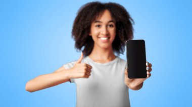 Nakit para, online alışveriş ve harika bir teklif. Pembe tişörtlü, kıvırcık saçlı, beyaz ekranlı akıllı telefonu gösteren ve menekşe arka planda izole edilmiş parmak uçlarını gösteren binlerce yıllık Afro-Amerikan kadını.