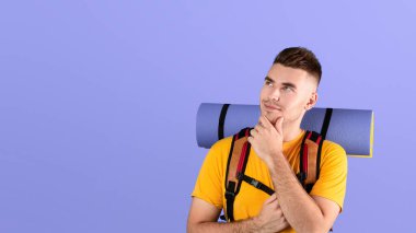 Sırt çantası ve turist paspası olan çekici bir gencin portresi mavi stüdyo arka planında çenesine dokunuyor. Bin yıllık düşünceli bir adam kamp malzemeleriyle yolculuğuna çıkmaya hazır.