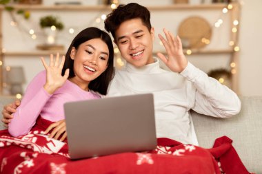 Noel Kutlaması İnternet 'te. Mutlu Asyalı çift dizüstü bilgisayarlarıyla Noel 'i kutluyorlar uzaktan kumandalı bir şekilde evlerinde oturup el sallıyorlar. Yeni Yıl ve Kış Tatili Konsepti