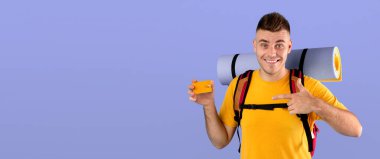 Seyahat bütçesi konsepti. Mavi stüdyo geçmişi üzerinden kredi kartına bakan turist ekipmanlı yakışıklı bir genç. Neşeli milenyum adamı kamp macerası için fon planlıyor.