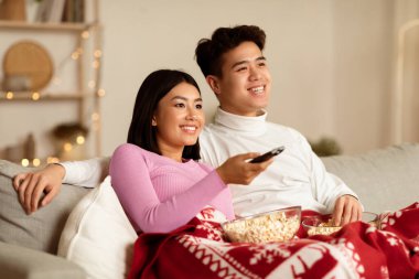 Asyalı eşler Noel arifesinde televizyon ve Xmas filmlerinin keyfini çıkarıyorlar evdeki oturma odasında koltukta oturuyorlar. Asyalı Aile İçeride Televizyon İzliyor. Yeni Yıl ve X-Mas Kutlama Kavramı