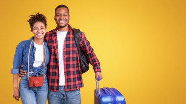 Valizli mutlu siyah gezginler stüdyoda sarı arka planda duruyor. Neşeli Turistler Seyahat, Turizm ve Tatil Gezisi Konseptine Hazır